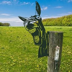 a wooden post with a drawing of a dog's head on it in the middle of a field