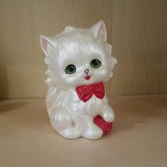 a white cat figurine with green eyes and a red bow on its neck