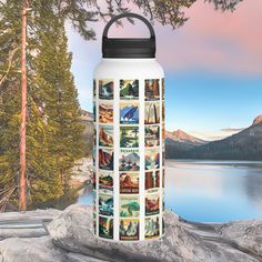 a water bottle sitting on top of a rock next to a body of water with trees and mountains in the background