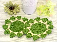 two crocheted coasters sitting on top of a table next to a flower