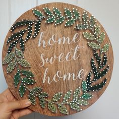 a hand holding up a wooden sign that says home sweet home with green leaves on it