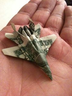 a dollar bill origami fighter jet in someone's hand