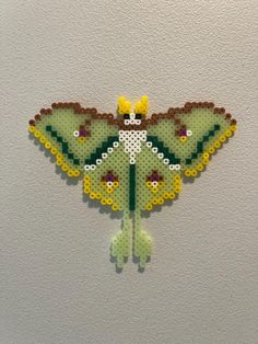 a green and yellow butterfly made out of legos on a wall next to a white wall