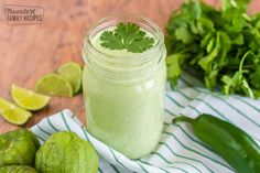 a green smoothie in a mason jar surrounded by limes and cilantro