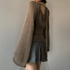 a woman standing next to a wall wearing a brown sweater and pleated leather skirt