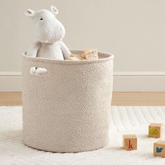 a stuffed animal sits in a large white storage bin with blocks on the floor next to it