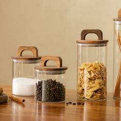 three glass containers filled with different types of food on a wooden table next to spices and cinnamon sticks