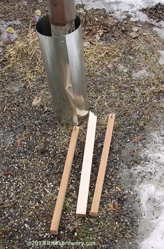 two pieces of wood are laying on the ground next to a metal pole with a wooden stick sticking out of it