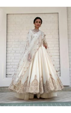 a woman standing in front of a brick wall wearing a white gown with gold detailing