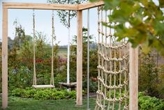 a wooden swing set with rope hanging from it's sides in a garden area