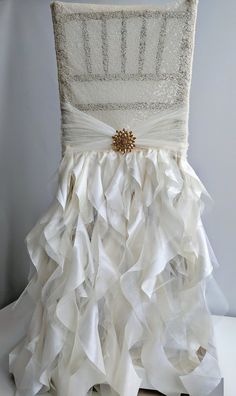 the back of a chair with ruffled white fabric and gold brooch on it