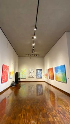 an empty room with paintings on the wall and wooden floors in front of white walls