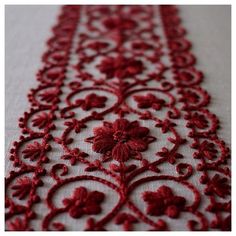 a red and white table runner with flowers on it's edge, in the middle of an embroidered design