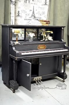 an old black piano is sitting in front of a curtained window with the eiffel tower behind it