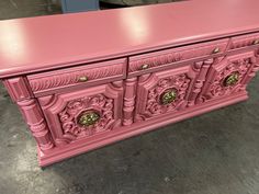 a pink dresser with ornate carvings on the front and sides, in a warehouse floor