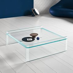 a glass coffee table sitting on top of a white floor next to a blue chair