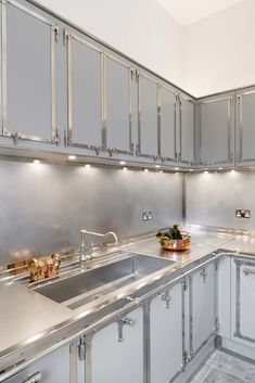 a kitchen with stainless steel counter tops and white cupboards on the wall, along with a bowl of fruit