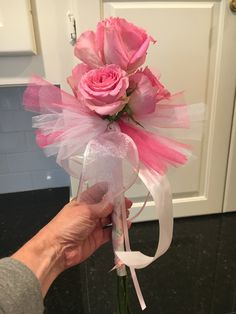 a person is holding a pink rose in a clear vase with white ribbon around it