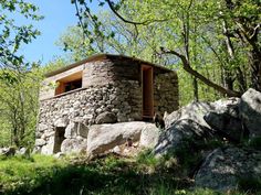 a small stone building sitting on top of a lush green hillside next to rocks and trees