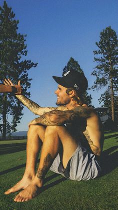 a man sitting in the grass with his arm wrapped around him and wearing a baseball cap