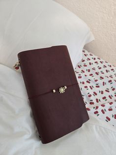 a brown notebook sitting on top of a bed next to a white comforter and pillow