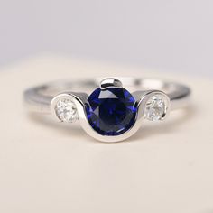 a ring with a blue sapphire and three white diamonds on the side, sitting on top of a table