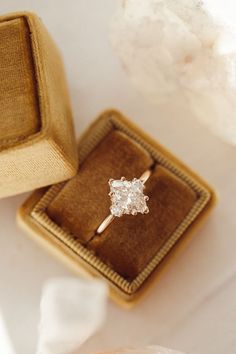 an engagement ring sitting on top of a cushioned box next to a white flower