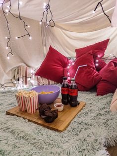 a bed with popcorn, soda and snacks on it in a room that has lights strung from the ceiling