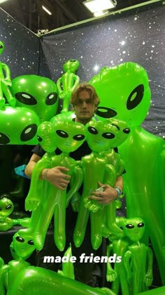 a man standing in front of an array of green alien balloons with faces on them