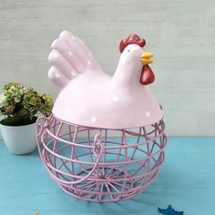 a pink chicken in a cage next to a potted plant