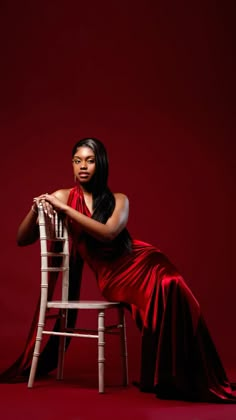 a woman in a red dress is sitting on a chair and posing for the camera