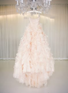 a dress hanging from a chandelier in front of a white wall with candles