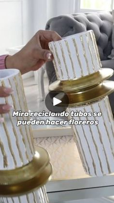 a person holding a white and gold cake on top of a metal stand in front of a couch