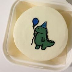 a birthday cake with a green dinosaur holding a blue balloon