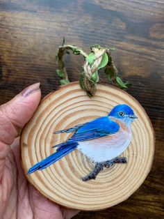 a hand holding a piece of wood with a blue bird on it