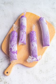 three popsicles on a cutting board covered in purple icing