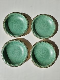 four green dishes sitting on top of a white table