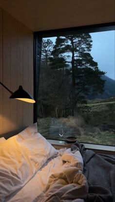 an unmade bed in front of a window with a view of the mountains outside