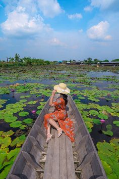 a woman wearing a hat sitting on top of a boat filled with water lillies