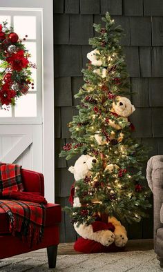 a christmas tree decorated with teddy bears in red and white stockings is next to a couch