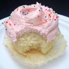 a cupcake with pink frosting and sprinkles on a white plate