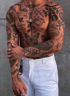 a man with many tattoos on his chest and arms is standing in front of a concrete wall