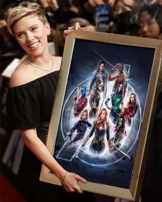 a woman holding up a framed poster in front of a group of people on the red carpet