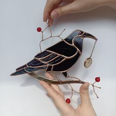 a hand holding a bird ornament with red berries on the side and another hand reaching for it