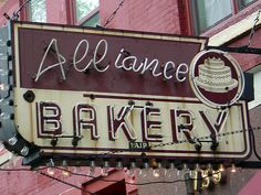 a sign for a bakery hanging from the side of a red brick building with lights strung around it