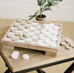 a wooden chess board with white pieces on it and a potted plant in the background