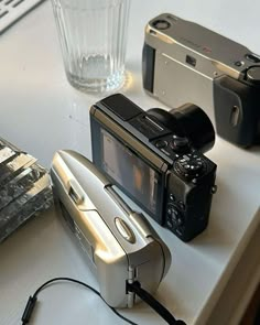 two cameras sitting on top of a table next to a glass and silver object in front of it