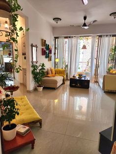 a living room filled with lots of furniture and plants on the floor next to windows