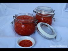 two jars filled with red sauce sitting on top of a white table cloth next to a small bowl