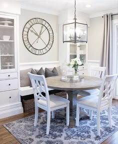 a dining room table with white chairs and a large clock on the wall above it